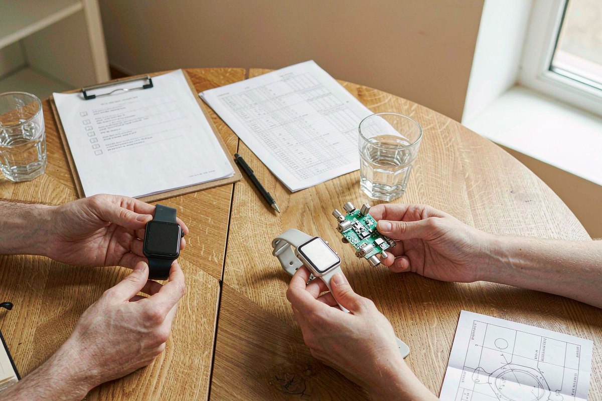 Two teams reviewing smart watch samples and supplier checklists on a meeting table